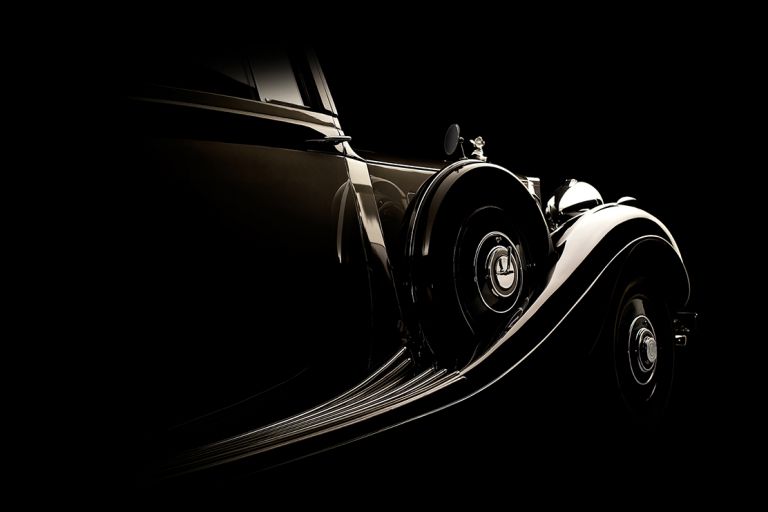 Seitlicher Blick auf den Kotflügel eines historischen Rolls-Royce vor schwarzem Hintergrund.