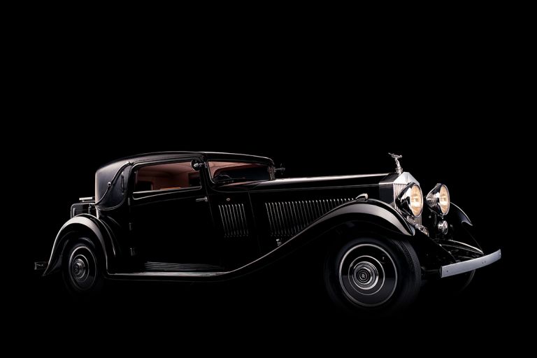 Seitenansicht eines historischen, schwarzen Rolls-Royce vor schwarzem Hintergrund
