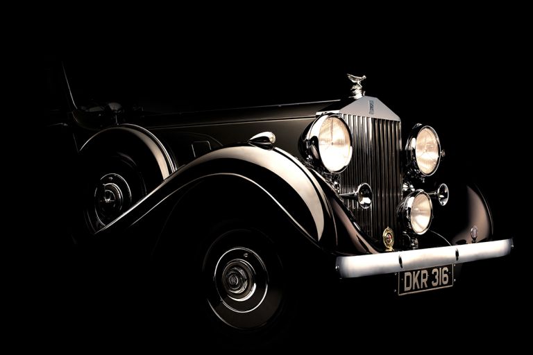 Seitliche Detailansicht der Front eines historischen Rolls-Royce vor schwarzem Hintergrund