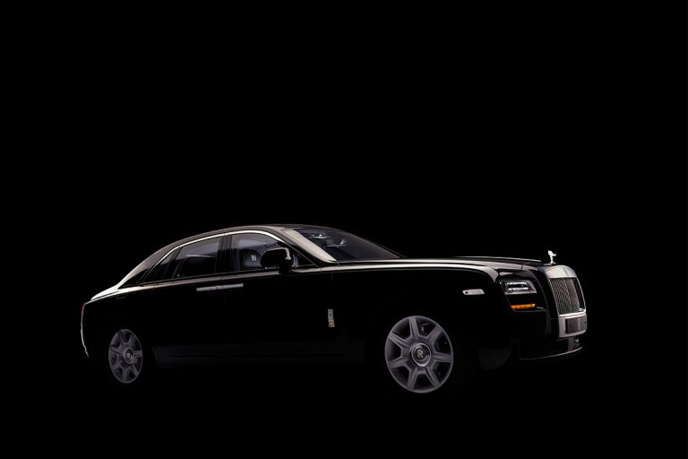 Diagonale Seitenansicht eines schwarzen Rolls-Royce vor schwarzem Hintergrund.