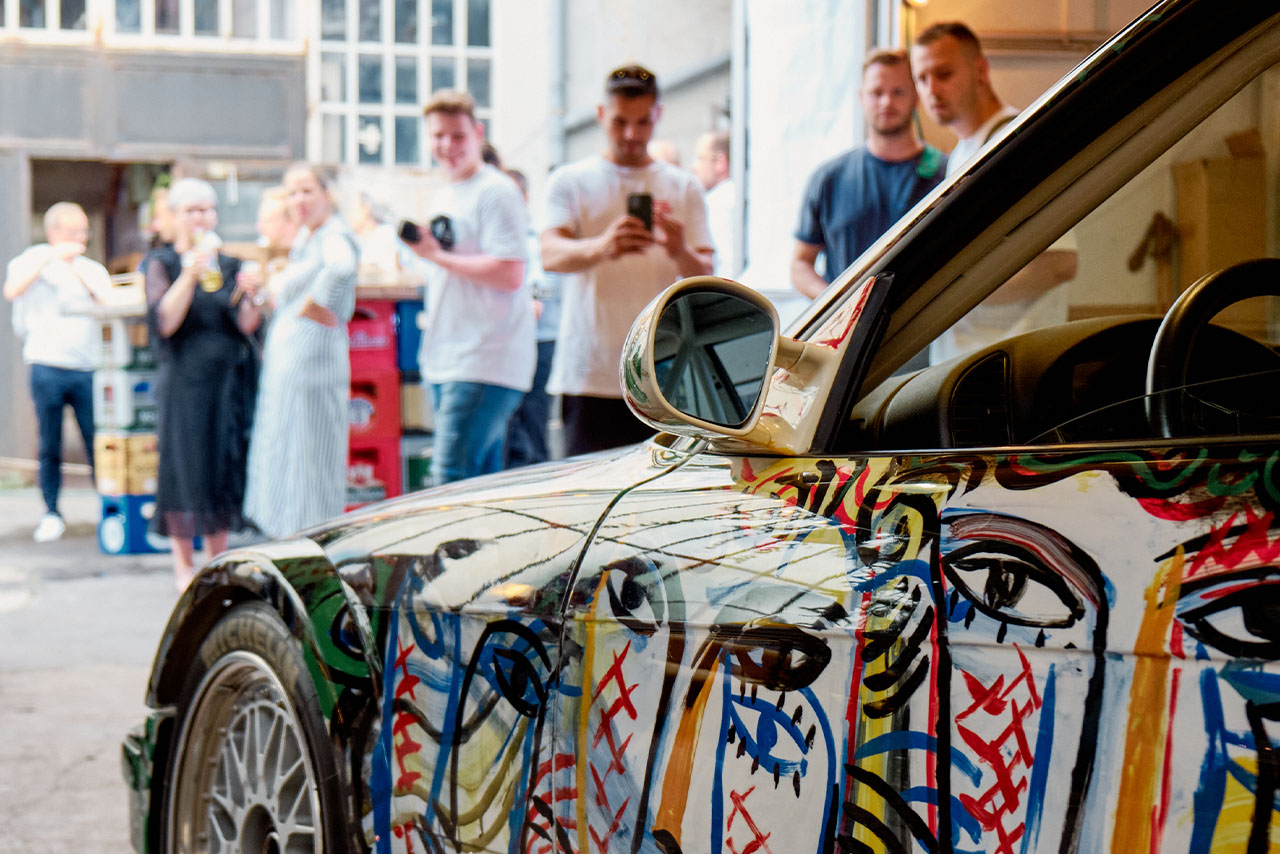 Ein bunt gestaltetes BMW Classic Auto parkt vor einer Gruppe von Menschen auf der Straße.