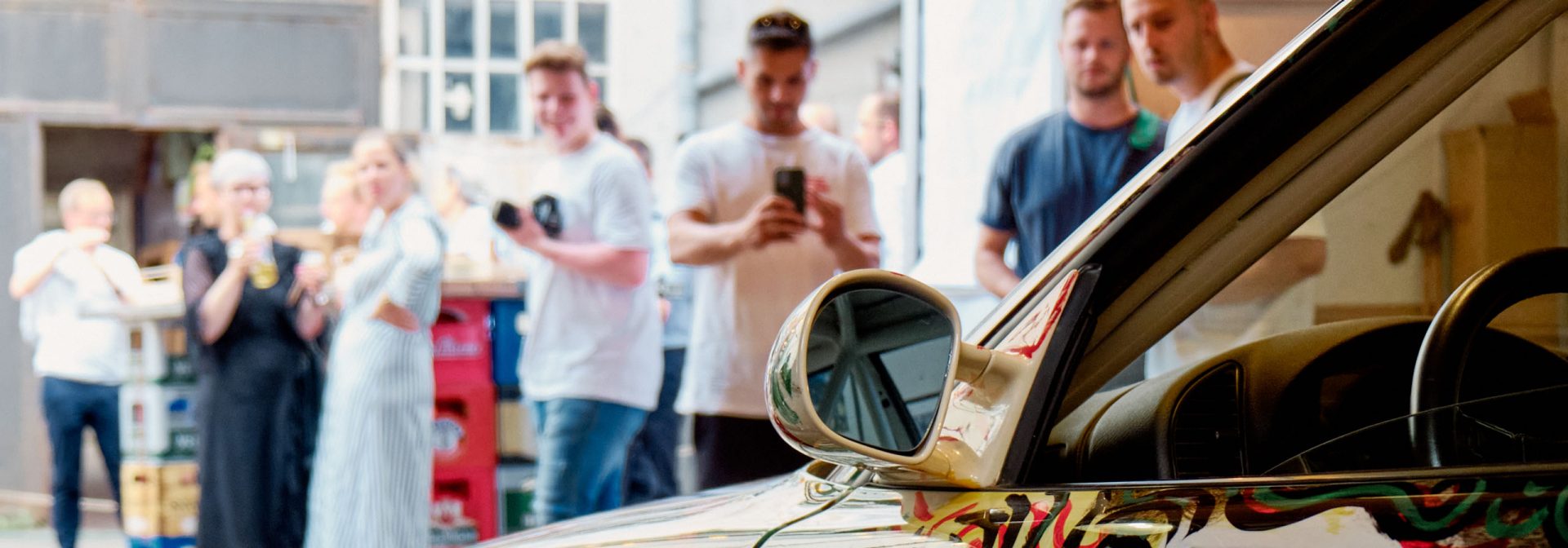Blick über ein BMW Art Car auf eine Besuchergruppe die teilweise das Fahrzeug fotografiert.