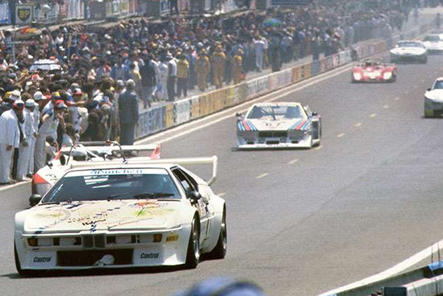 Packende Rennszene aus den 80er Jahren mit einem weißen BMW M1 im Vordergrund.