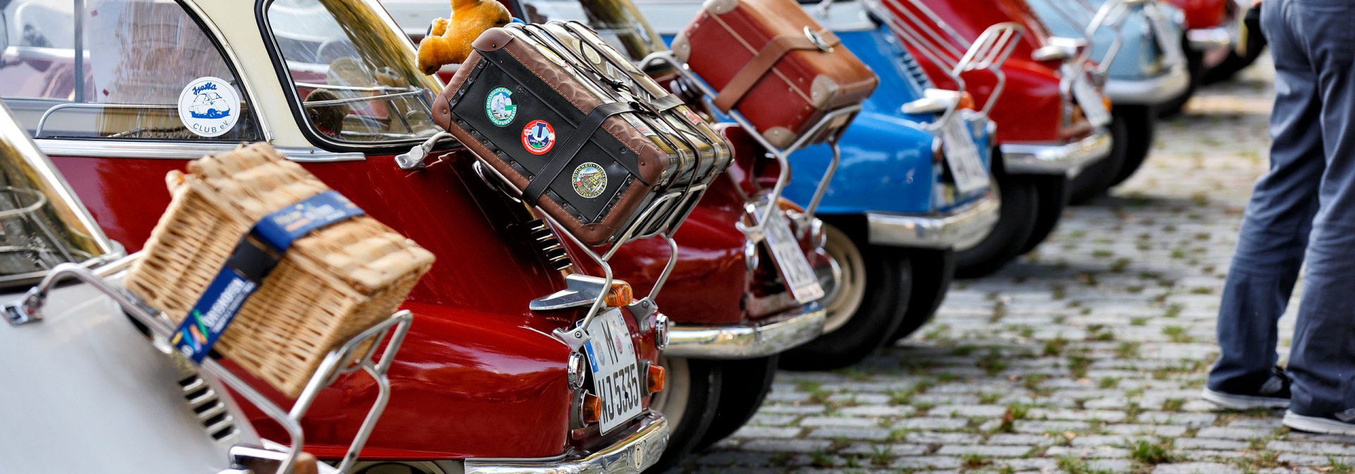 Bunte Sammlung von BMW Isetta, die auf einem Event in Reihe präsentiert werden und auch wegen ihrer individuellen Gepäcklösungen begeistern.