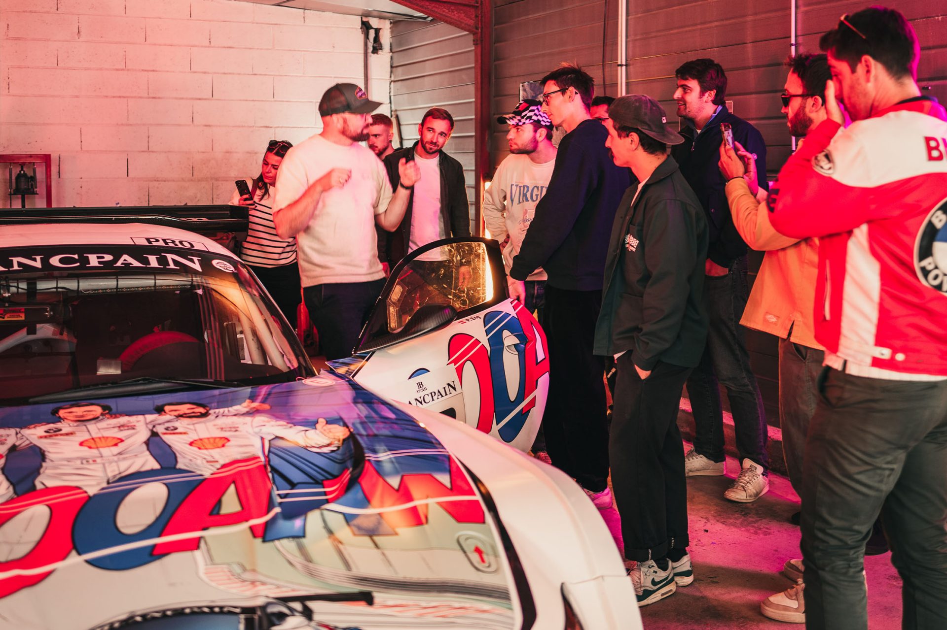 Eine Gruppe junger Männer lauschen einem Guide der gerade etwas zu einem BMW aus dem Rennsport erklärt.