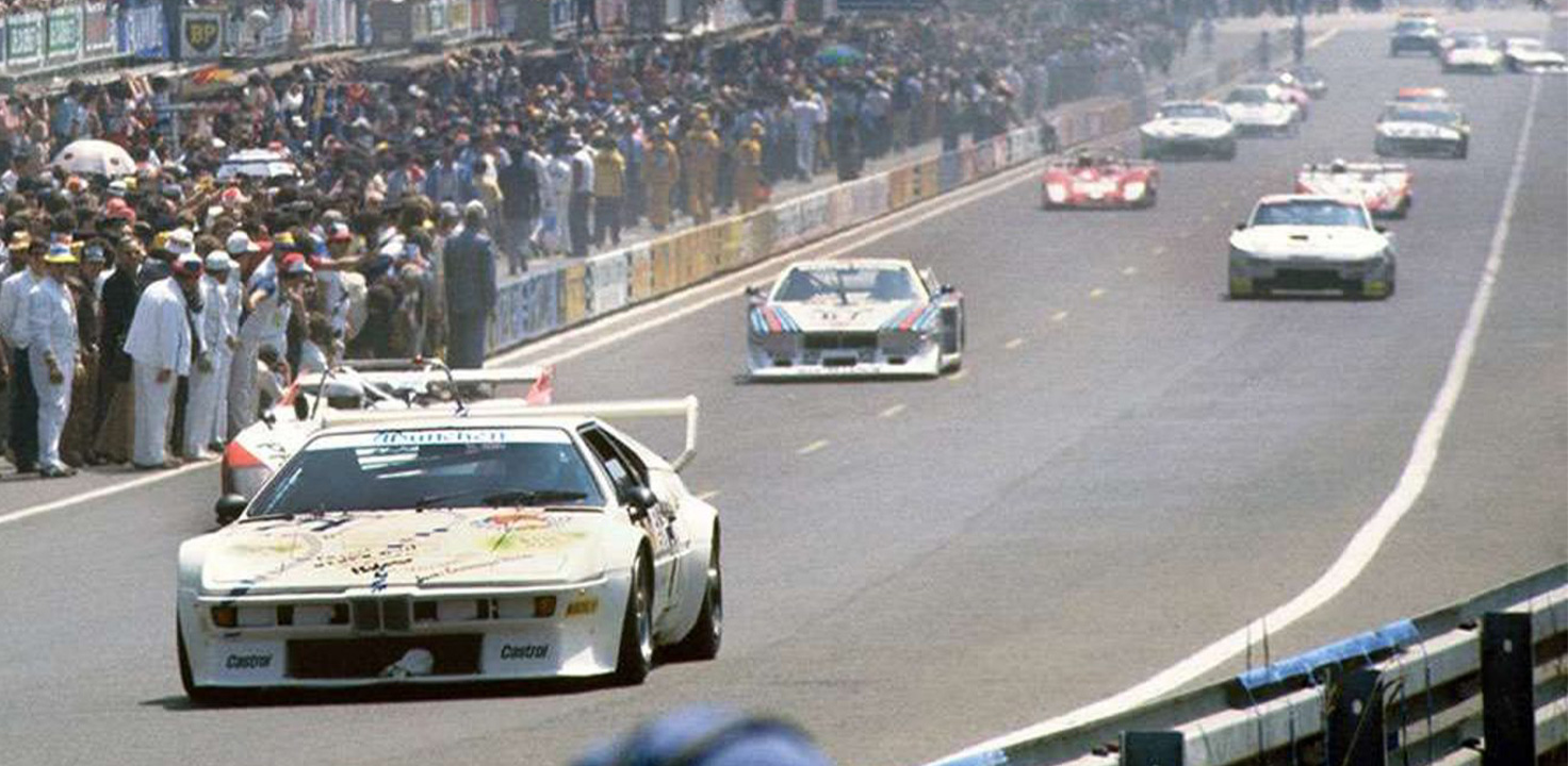 Packende Rennszene aus den 80er Jahren mit einem weißen BMW M1 im Vordergrund.