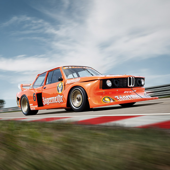 Orangener BMW 320 Gruppe 5 Rennwagen im Einsatz auf der Rennstrecke.