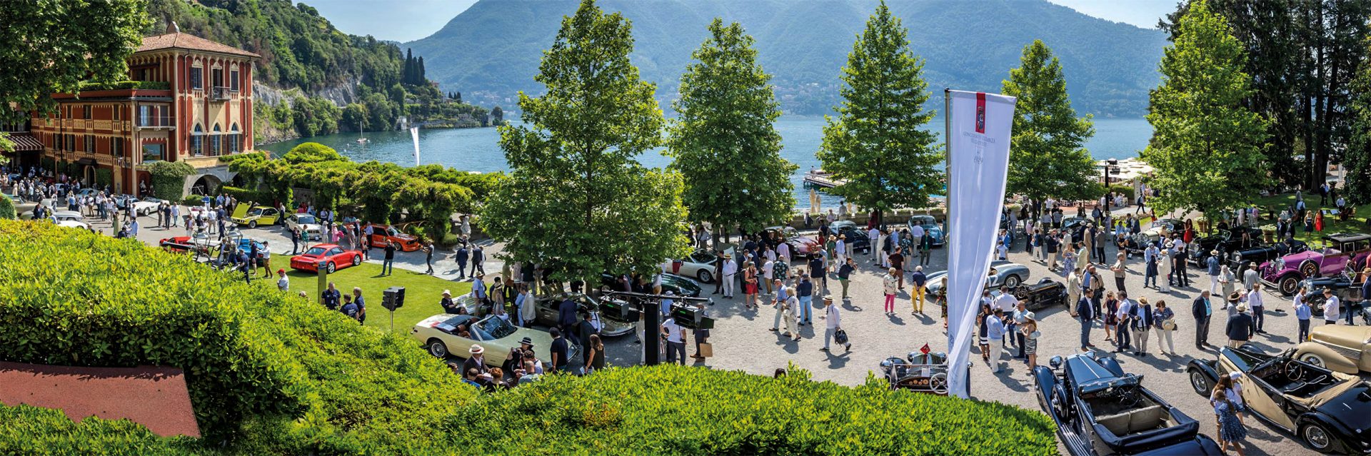Oldtimer und ihre Besitzer auf dem Parkplatz vor dem Hotel Villa d’Este mit See und Bergen im Hintergrund