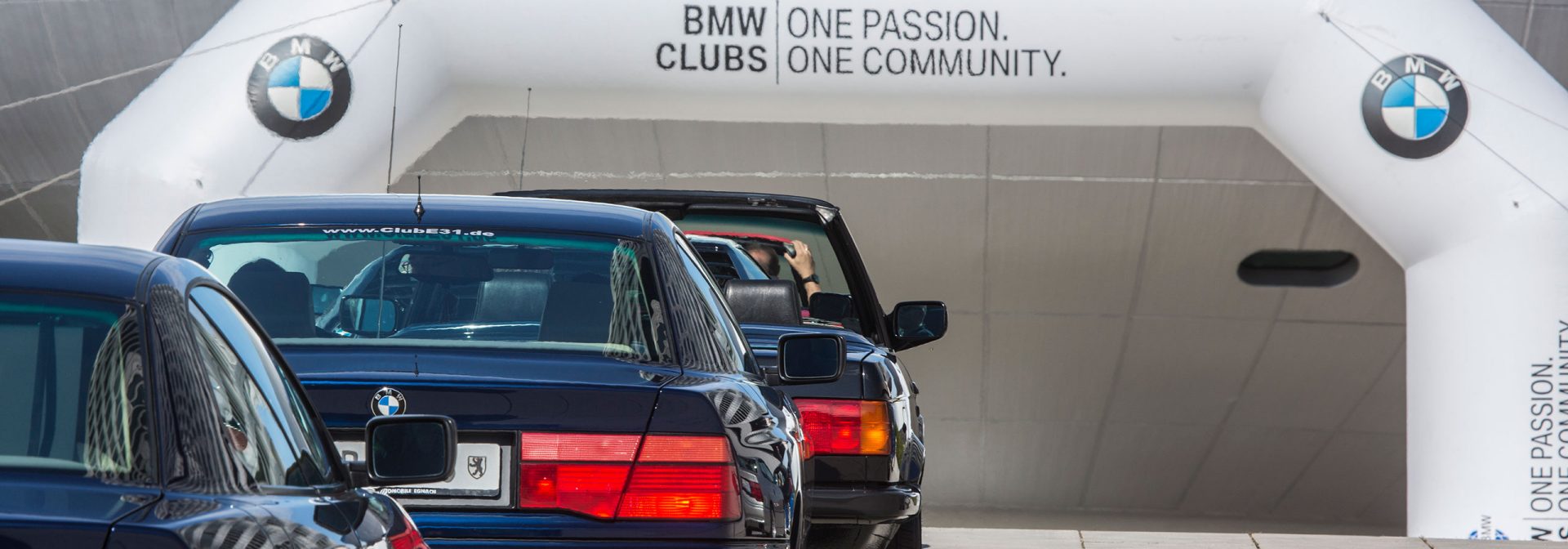 Mehrere BMW Youngtimer die vor einem Portal des BMW Clubs stehen, der vor dem BMW Museum in München aufgestellt ist.