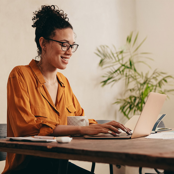  Frau mit Brille, die fröhlich an ihrem Laptop arbeitet.