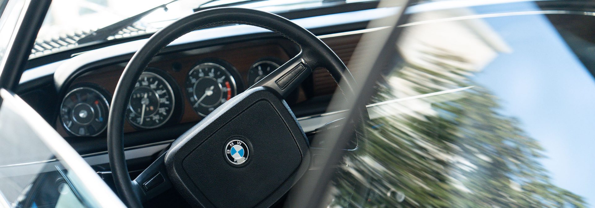 Lenkrad und Dashboard eines BMW Classic Fahrzeugs, die die Instrumente und Bedienelemente für den Fahrer darstellen.