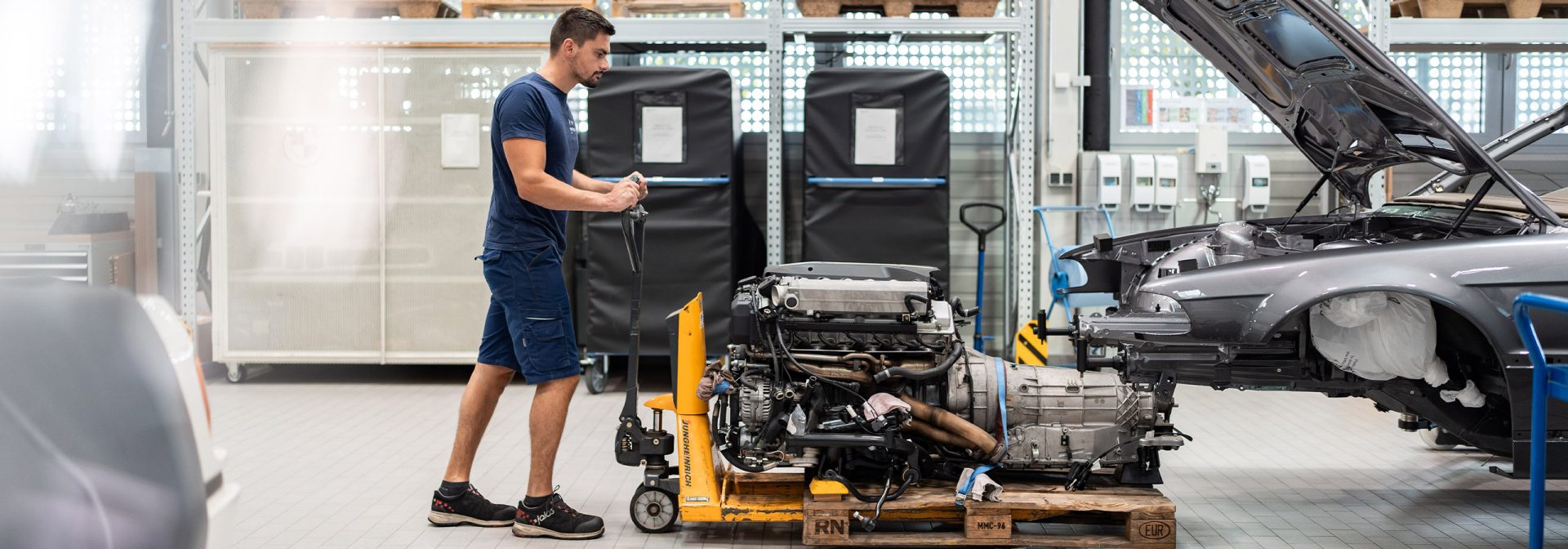 Ein Mechaniker führt den Motor eines historischen BMW Fahrzeugs mithilfe eines Wagens an die Karosserie