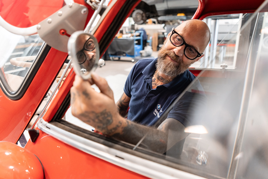 Ein Mann mit Brille und Tattoos arbeitet an der Reparatur eines Classic Fahrzeugs.