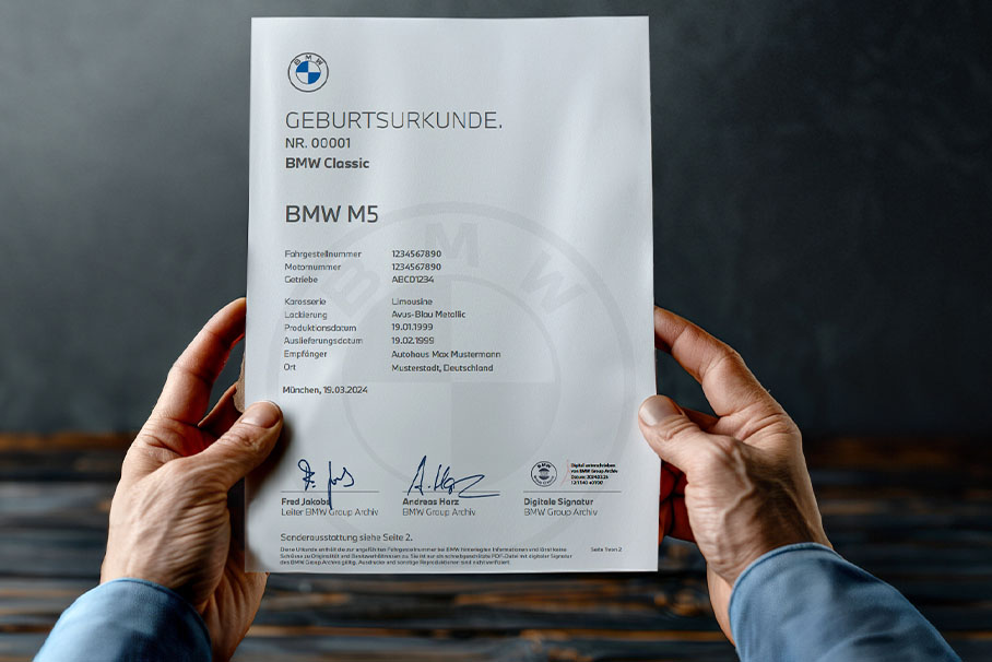 Zwei Hände halten das Zertifikat für Fahrzeugsdaten eines BMW M5.