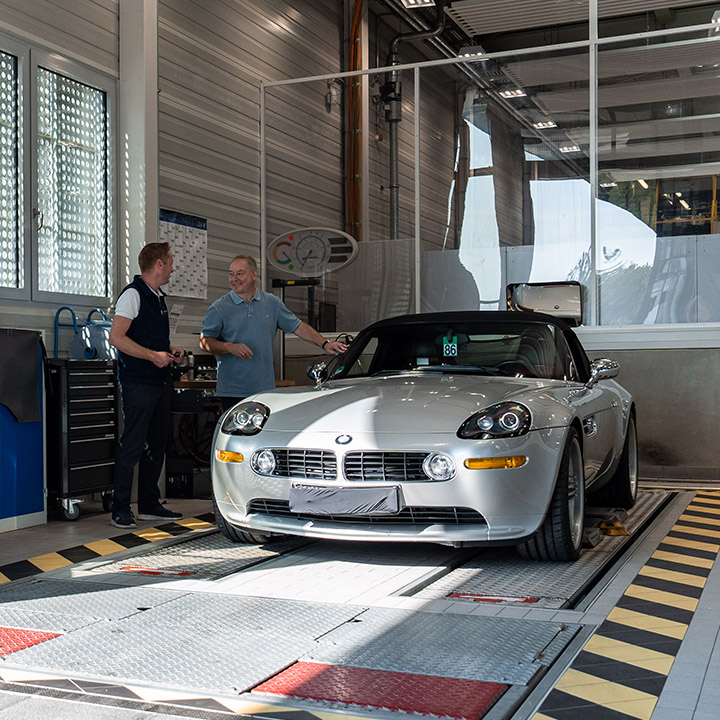 Zwei Männer unterhalten sich in einer BMW Classic Garage, umgeben von verschiedenen Werkzeugen und einem BMW Modell.