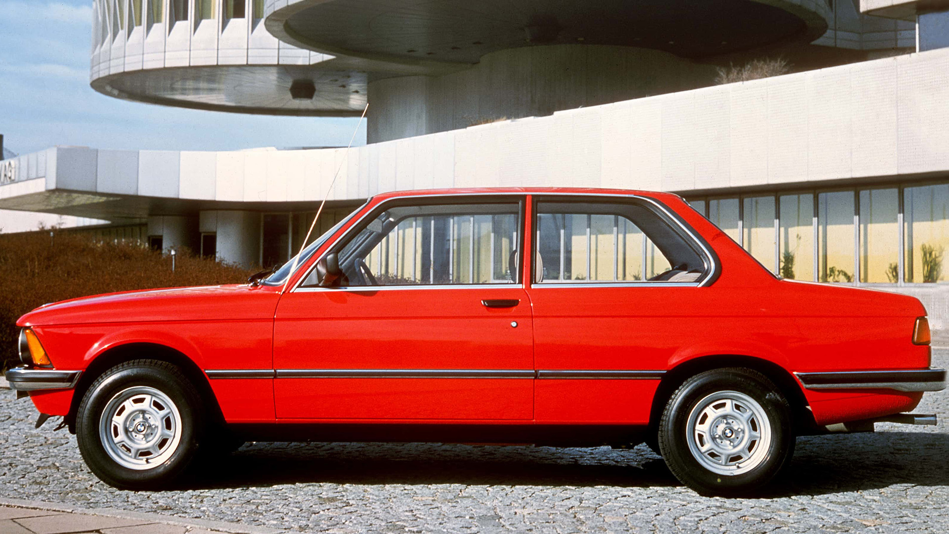 Seitenansicht eines roten 3er BMW der ersten Generation vor dem BMW Vierzylinder.