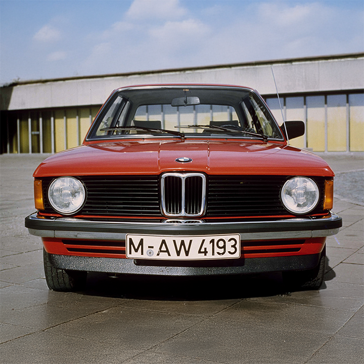 Frontansicht eines 3er BMW der ersten Generation vor dem BMW Vierylinder Gebäude.