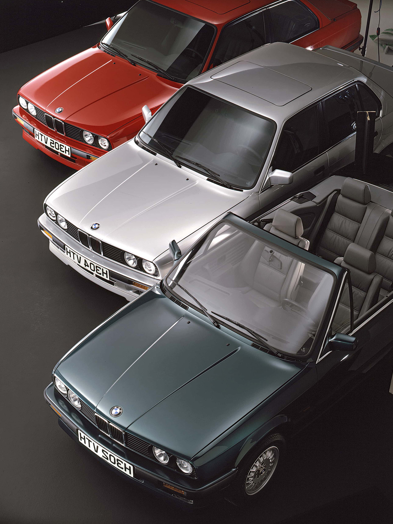Drei 3er BMW der zweiten Generation in rot, silber und grün nebeneinander geparkt.