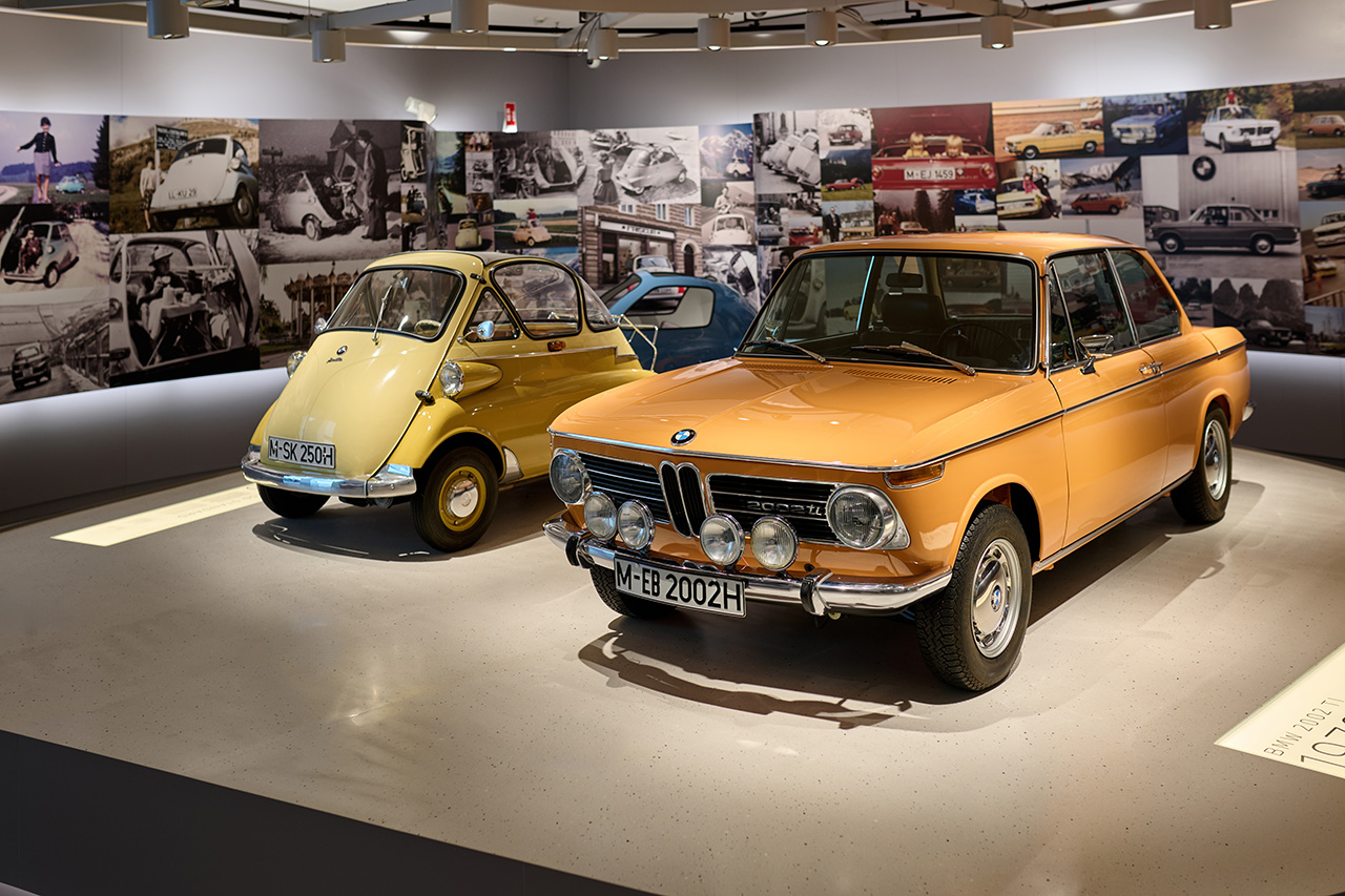 Im BMW Museum werden BMW-Fahrzeuge ausgestellt, umgeben von Bildcollagen an den Wänden.