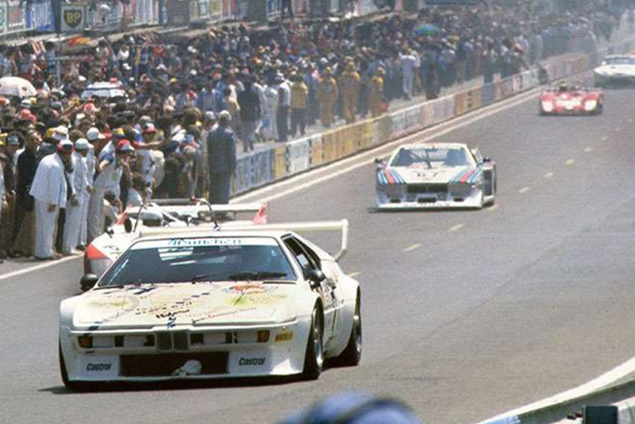 Packende Rennszene aus den 80er Jahren mit einem weißen BMW M1 im Vordergrund.