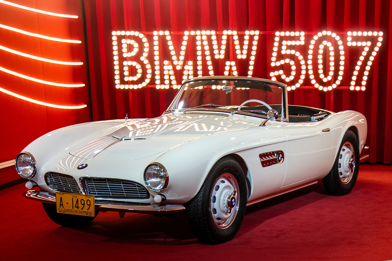 A white BMW sports car is on display in front of a red curtain.