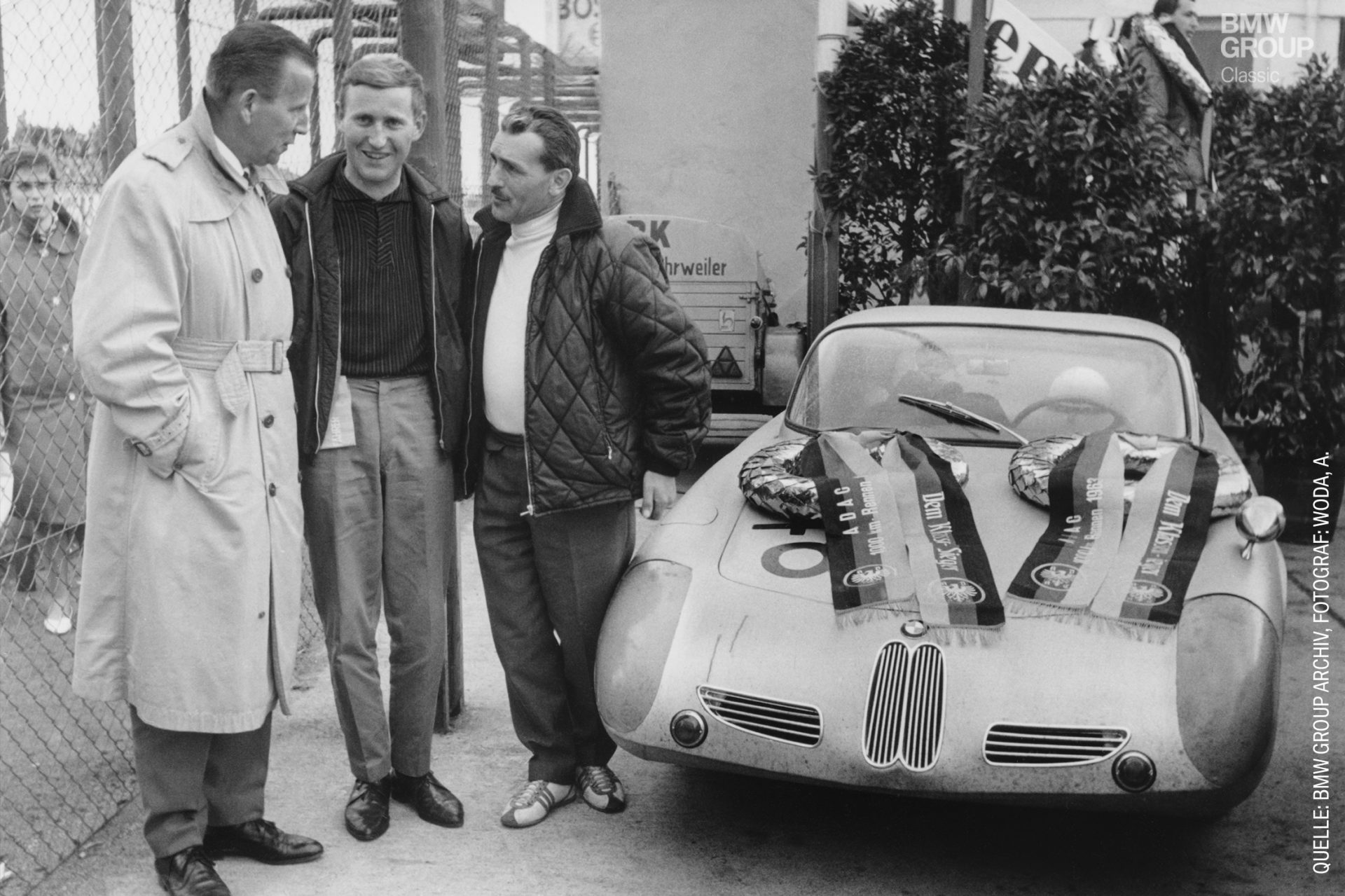 Three men are standing next to a BMW 700