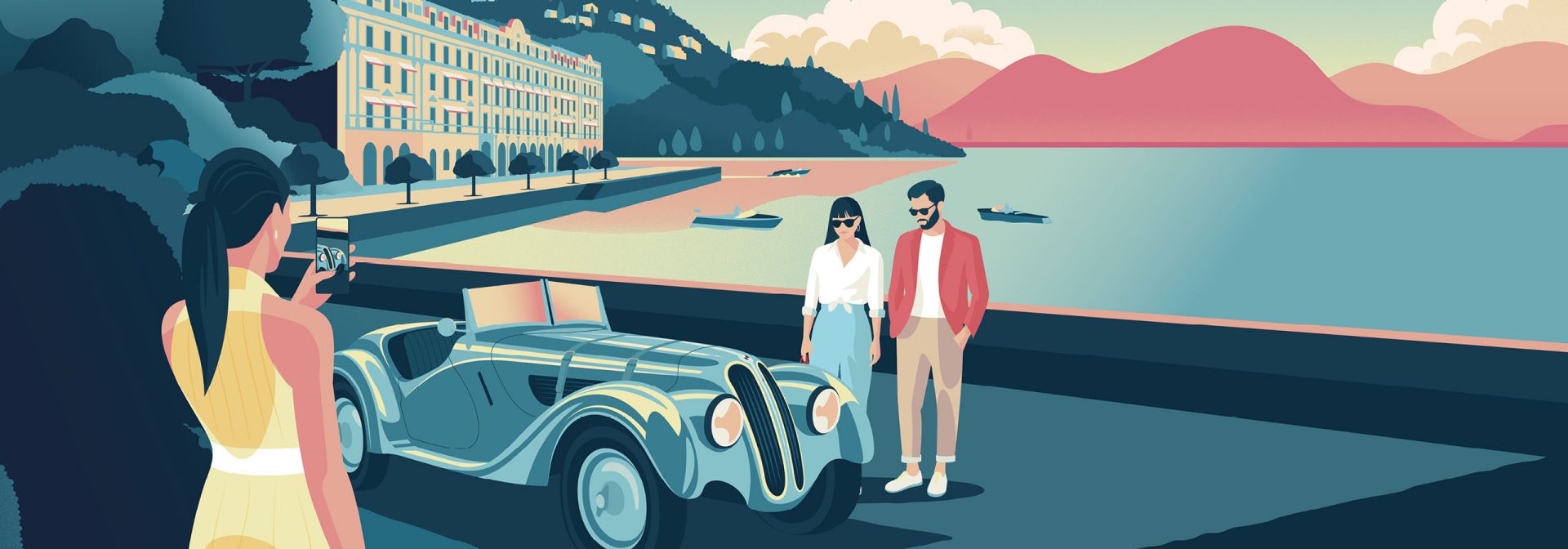 A woman in a yellow dress is photographing a couple in front of a classic car on a waterfront promenade, with mountains and water in the background.