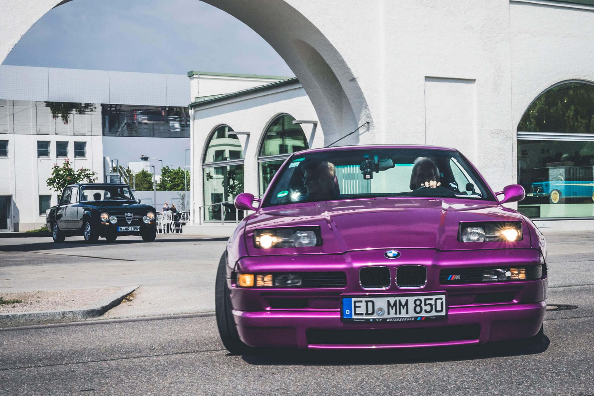 A purple BMW 6 Series classic with the typical pop-up headlights leaves the BMW Group Classic gate.