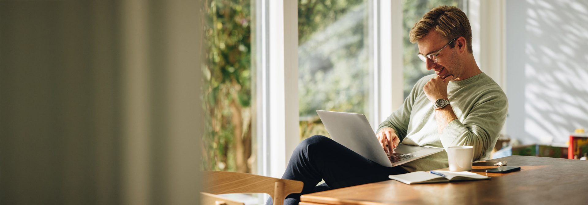 Sitting at a table, a man is working on his laptop.