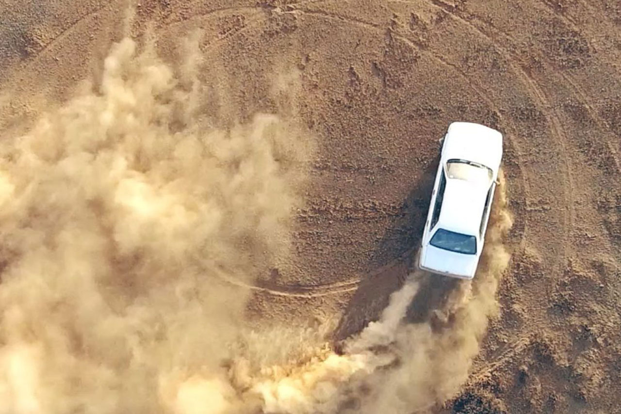 An aerial view of a car driving through dust shows the movement and the dust clouds around the vehicle.