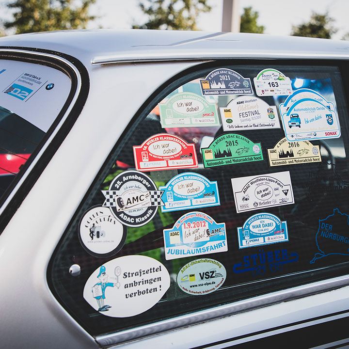 A classic BMW with numerous stickers on the rear side window, as a reminder of classic car events of recent years.
