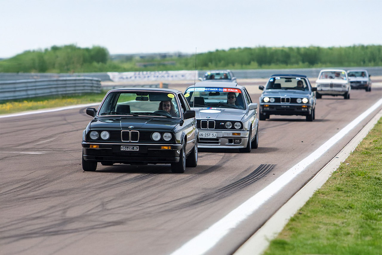 A group of BMW 3 Series Classic vehicles of different model years drive relaxed one after the other on a race track.