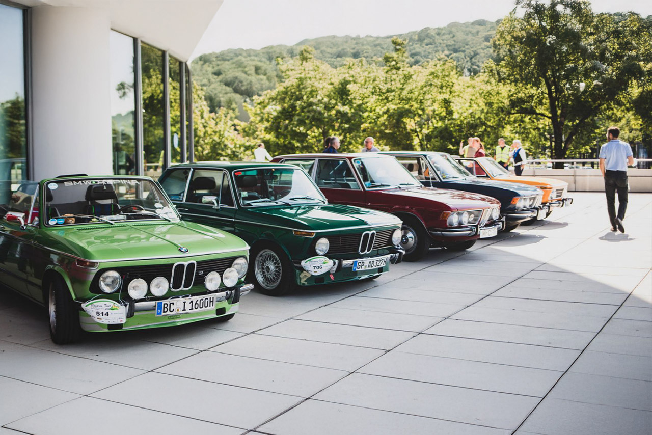 BMW Classic cars are lined up in front of a historic building, giving the scene a charming character.