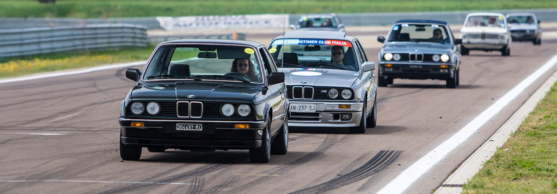 A group of BMW Classic vehicles drives along a road surrounded by a picturesque landscape.