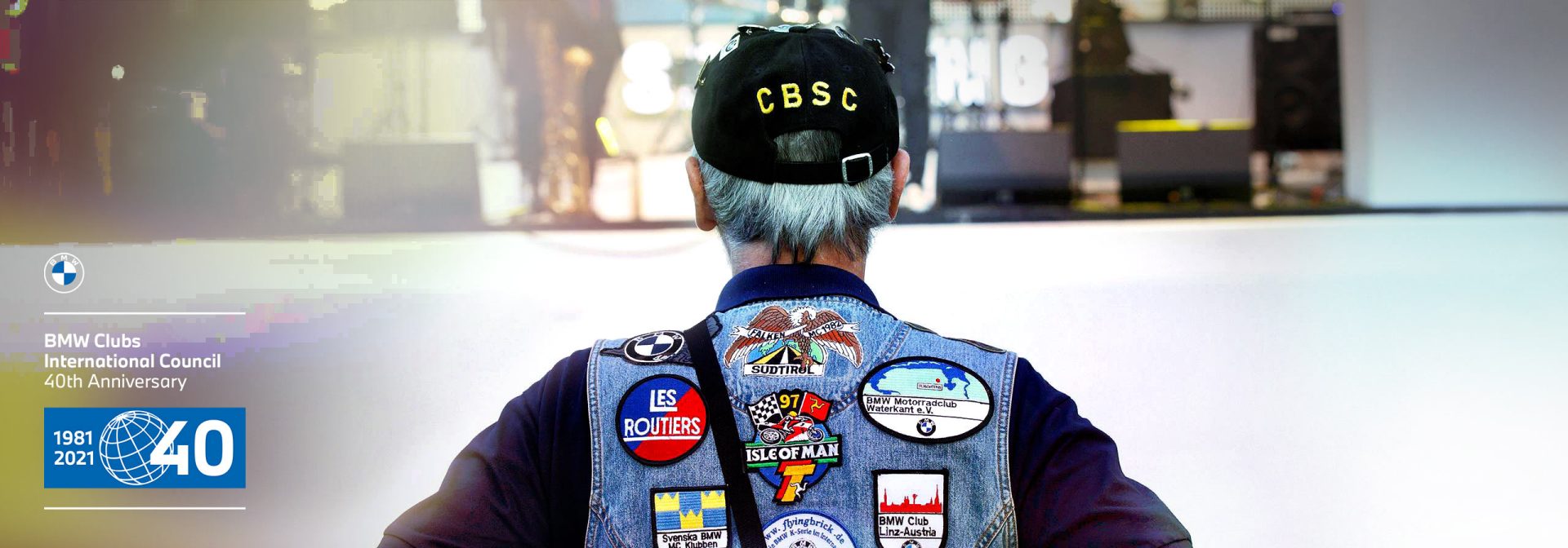 A man wears a hat and a jacket with patches that emphasize his individual style.