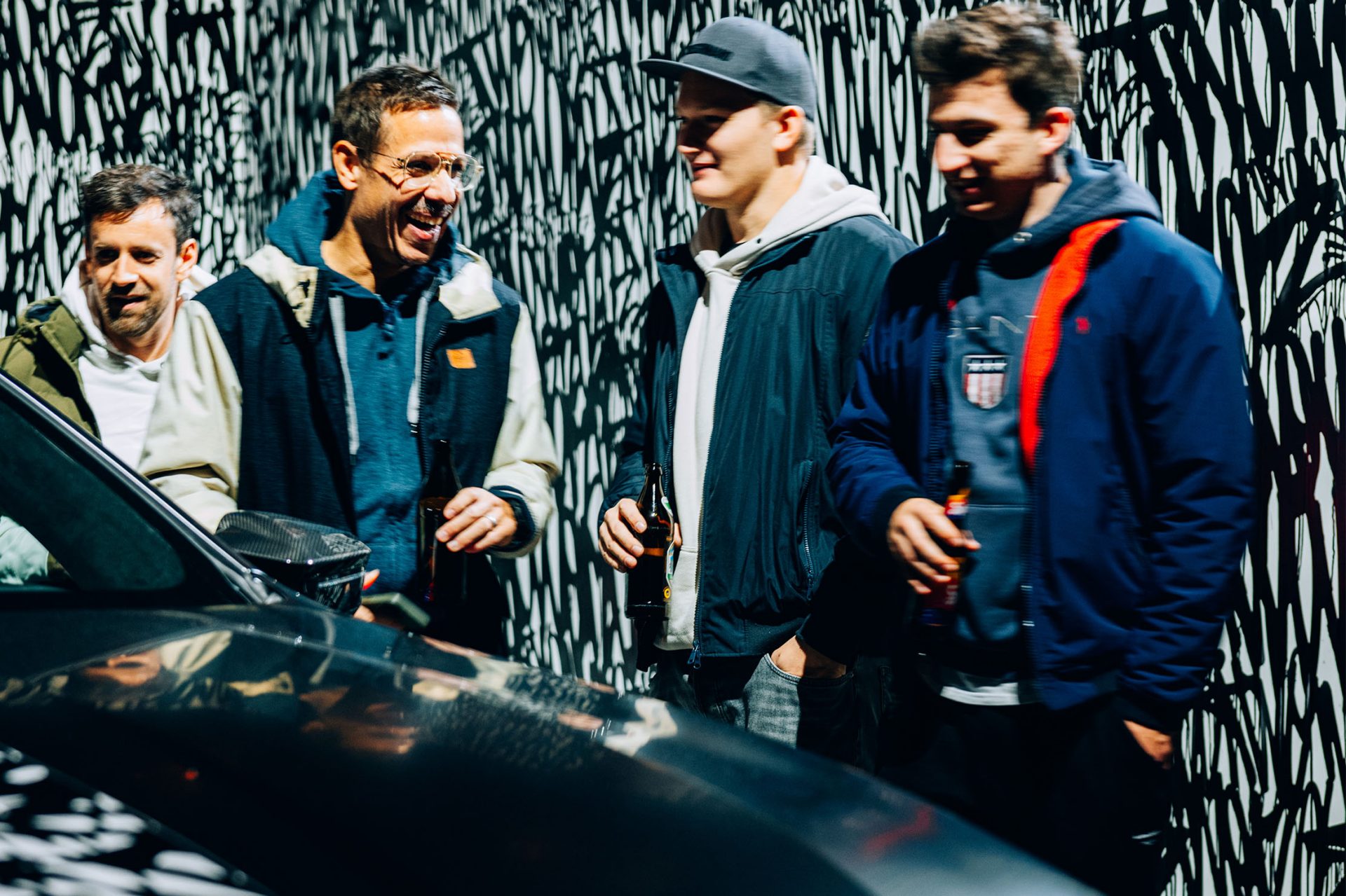 Four young, cheerful BMW fans chatting about cars in front of a dark BMW.