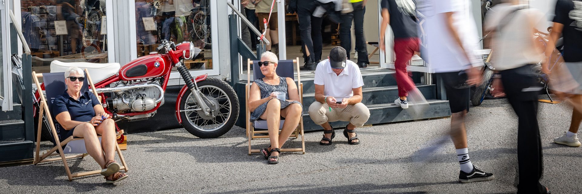 People sit on chairs in front of a BMW motorcycle and enjoy the surroundings.