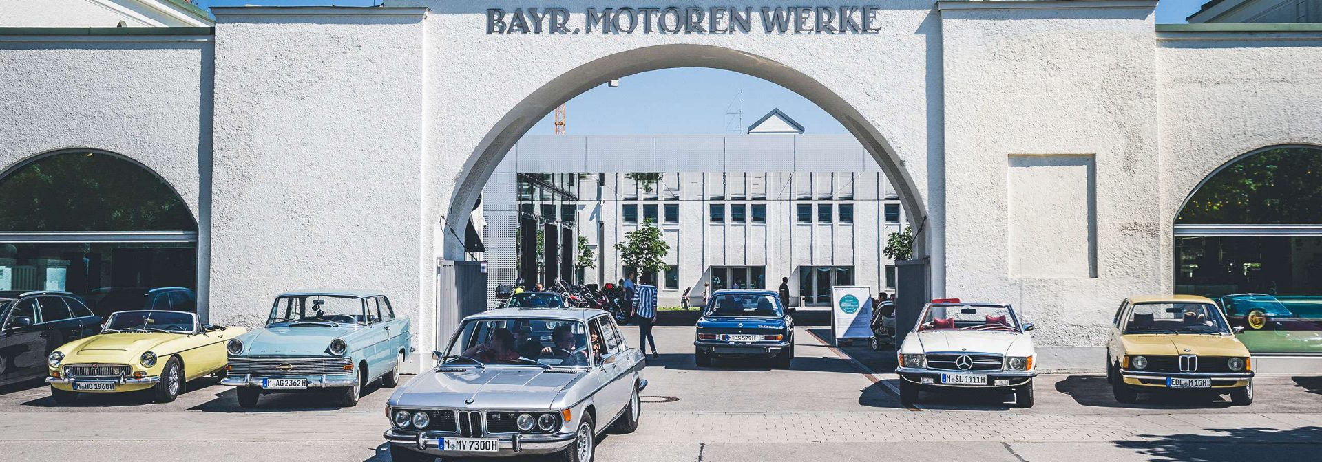 Numerous classic cars of different brands in front of the portal of the oldest BMW plant in Munich, which now houses the BMW Museum.