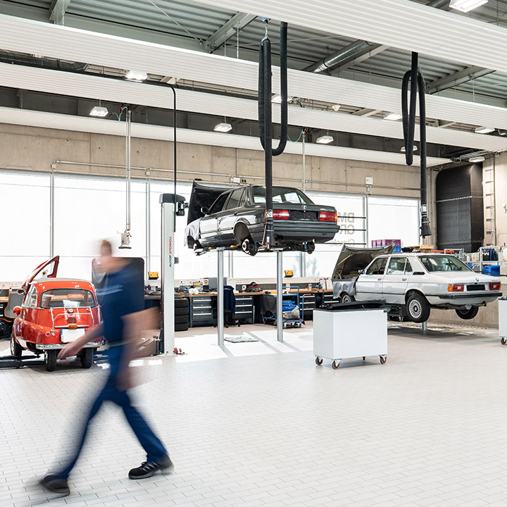 Three historical BMW vehicles on car lifts in a workshop.
