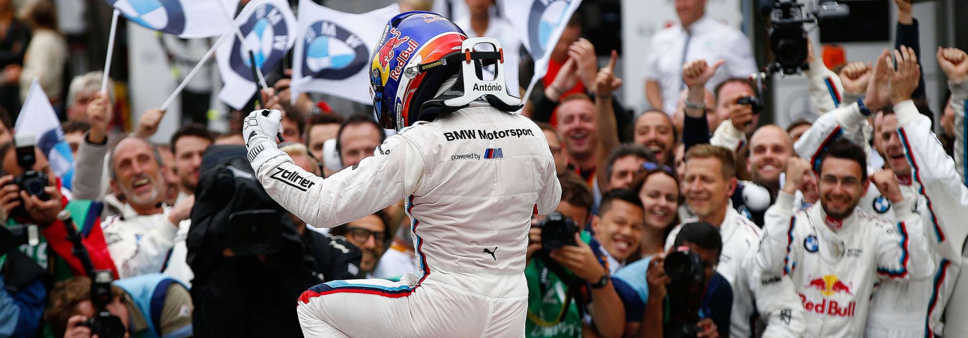 BMW racing driver in winning pose on the car in front of cheering fans.