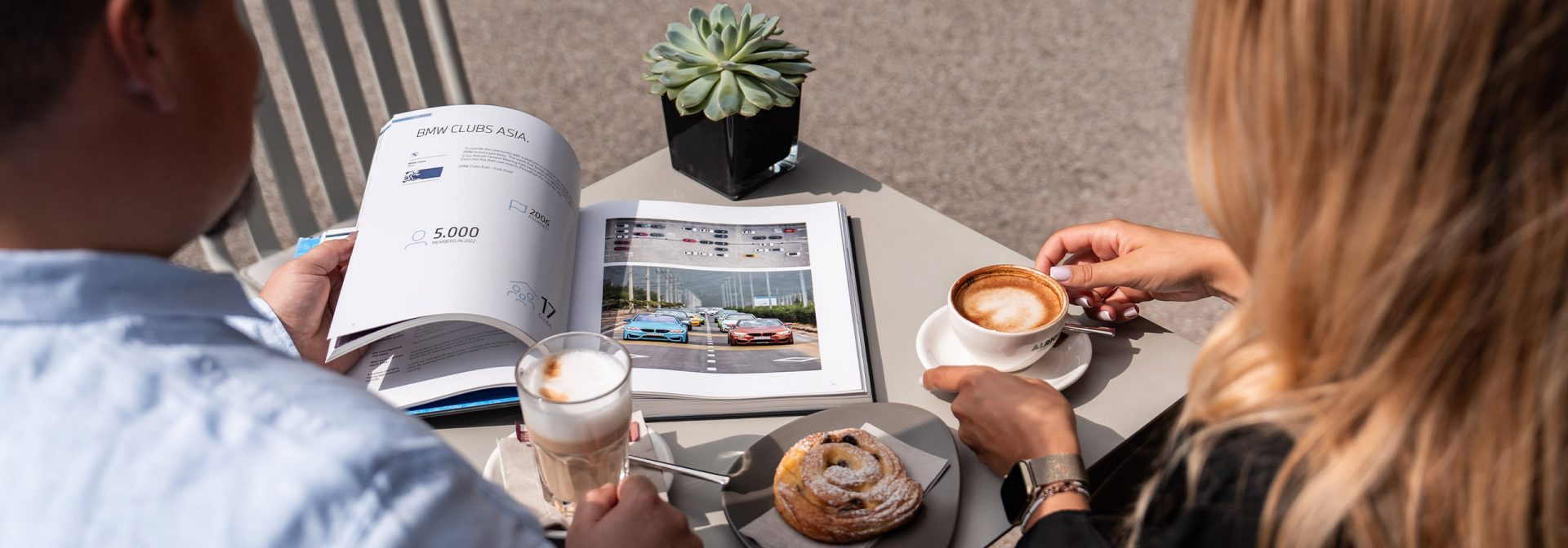 Two people are sitting in the BMW Classic Cafe drinking coffee.
