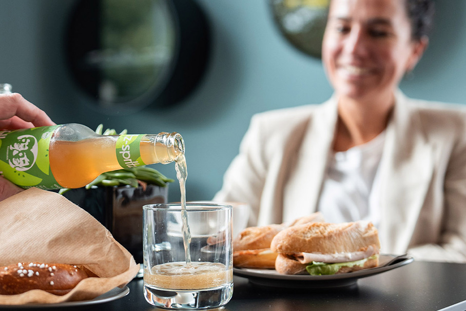 Two young women and a man at breakfast - one pours the other an orange juice.