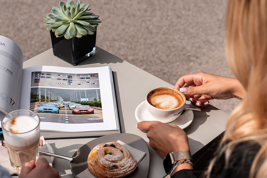 A young couple drinking coffee. He has a latte macchiato in his glass, she has a cappuccino in her hand.