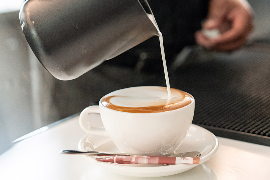 Using milk from a small pitcher, a barista conjures up a small work of art to enjoy.