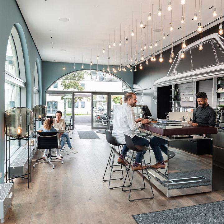 A view inside the BMW Classic Café with guests at the bar and tables, and a barista behind the counter.