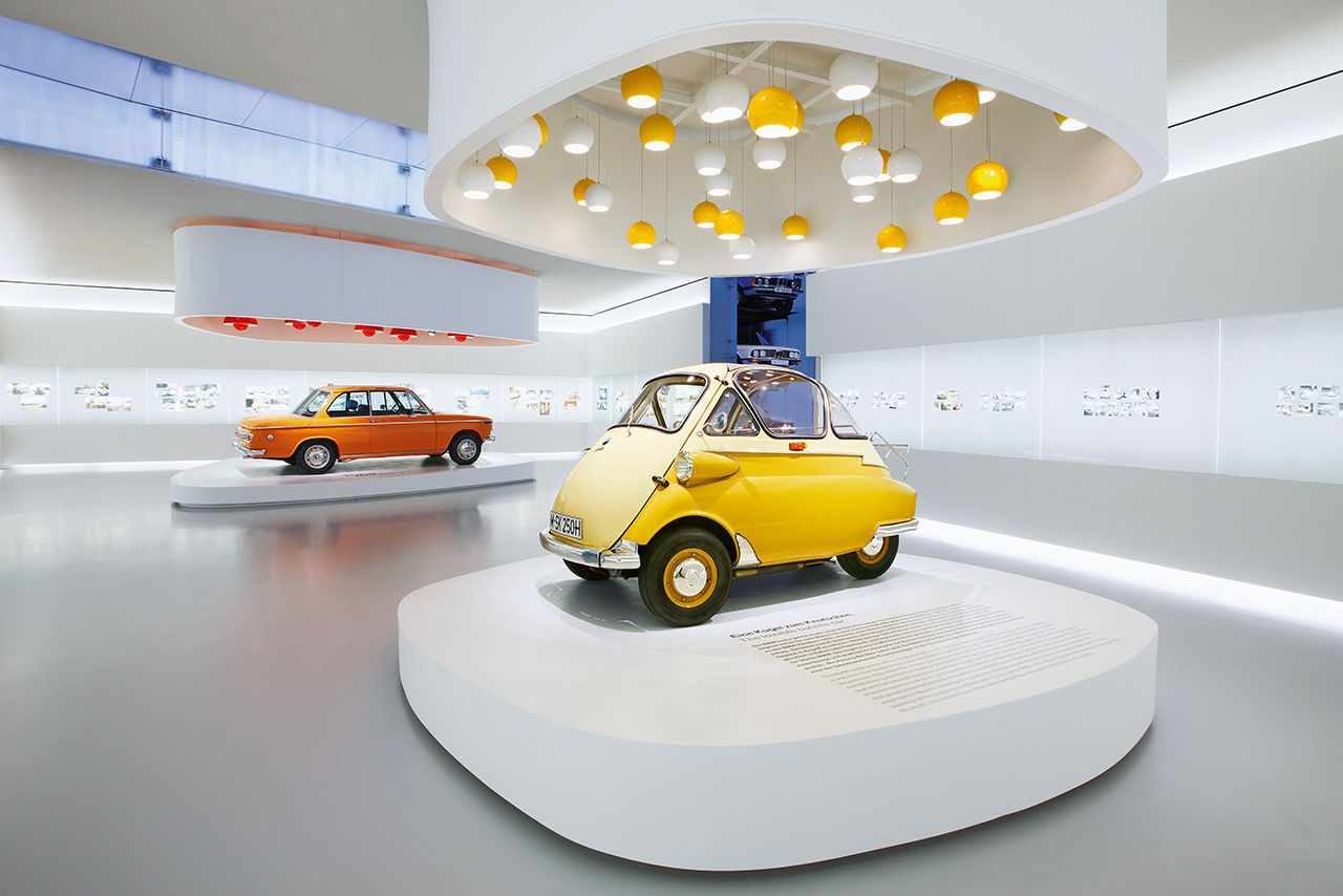 A small car is on display in the BMW Museum, surrounded by informative panels and other exhibits.