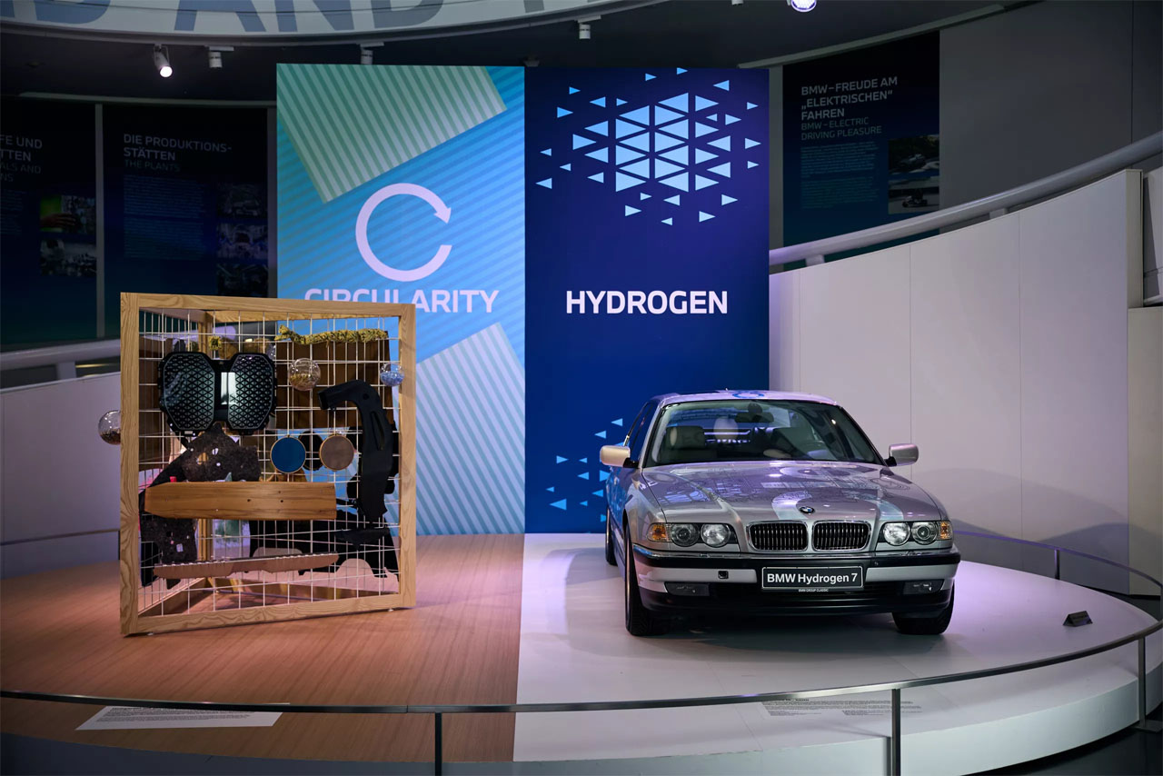 A historic BMW car is on display in a museum, surrounded by visitors admiring the details.