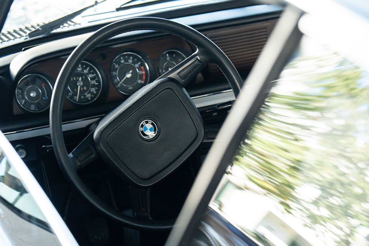 View through the open driver's door onto the steering wheel and dashboard of a vehicle.