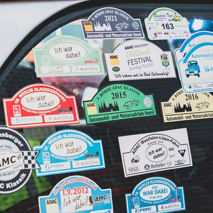 13 Stickers on the window of a car. Each one is for a drifferent rallye the car participated in.