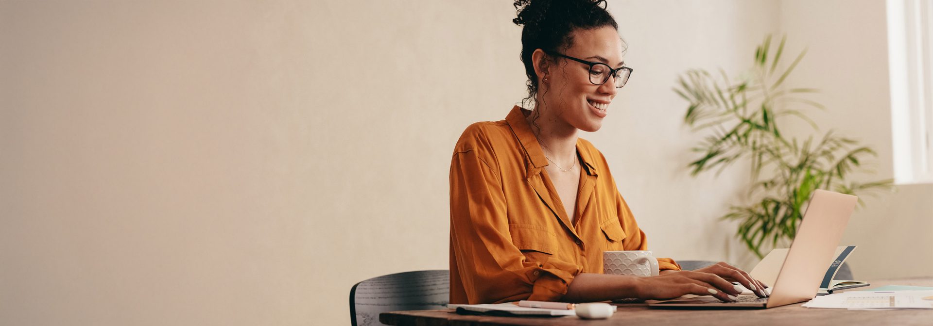  Woman with glasses and a orange shirt, happily working on her laptop.